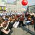 Große Orchesterprobe im Freien mit vielen Musikern, die Streichinstrumente wie Violinen und Celli spielen. Ein Dirigent steht vor den Musikern und leitet das Orchester.