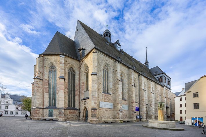 Großes historisches Kirchengebäude mit gotischen Architekturmerkmalen wie spitzen Bögen, hohen Fenstern und einem steilen Satteldach, aufgenommen von außen bei Tageslicht.