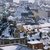Ein Bild einer verschneiten StadtAvec historischen und klassischen Gebäuden, wobei besonders eine charaktervolle Kirche mit grünem Turm und spitzem Dach im Vordergrund sichtbar ist.