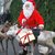 Ein Mensch verkleidet als Vater Weihnachtsmann, der zwei Rentier führten und ein Geschenk mit rotem Band auf einem Schlitten trägt.