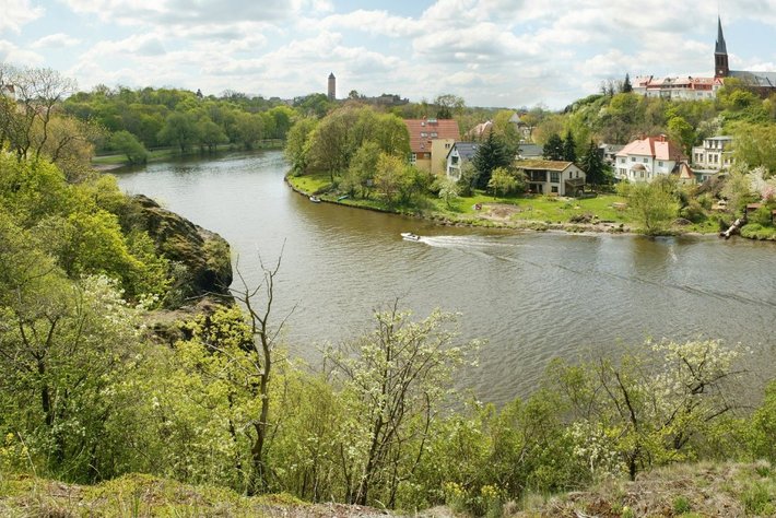Diese Landschaft zeigt einen ruhigen Fluss, der sich durch Grünland schlängelt. Am Ufer stehen Häuser, die sich über einen sanft ansteigenden Hügel erstrecken. Wider absatz zeigen Baumbestand und Felspartien.

Alternativtext: 