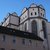 Gotische Kirche mit zwei markanten Rundtürmen, hohem Mittelschiff und großen, spitzbogigen Fenstern, darunter ein großes Rosettenfenster. Hell verputzte Fassade mit dunklem Dach.