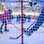 Ein Kind in Sportkleidung spielt Eishockey auf einer Eisfläche. Im Vordergrund liegt ein Schläger auf dem Eis, während im Hintergrund weitere Spieler und Zuschauer zu sehen sind.