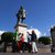 Éine Gruppe von vier erwachsenen Menschen steht vor einer Bronze Statue eines Mannes auf einem altasartigen Sockel an einem sonnigen Platz.
Die Statue scheint bedeutend oder historisch zu sein und hierfür bilden sie eine geschlossene Gruppe.