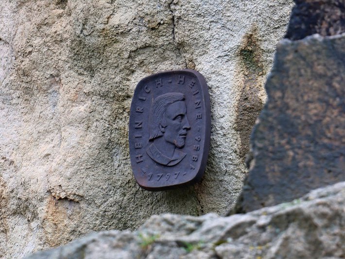 Altar oder Gedenktafel aus Stein mit eingraviertem oder erhabenem Symbol, das eine stilisierte Person oder Figur in sitzender Position zeigt, möglicherweise ein historisches oder kulturelles Zeichen an einer alten Mauer.