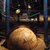 Alter Globus aus Holz oder Metall mit eingravierten Kontinenten und Ozeanen, der auf einem Ständer ruht. Im Hintergrund ein historisches Modell mit Planeten und Sonne, umgeben von einem Metallgitter.