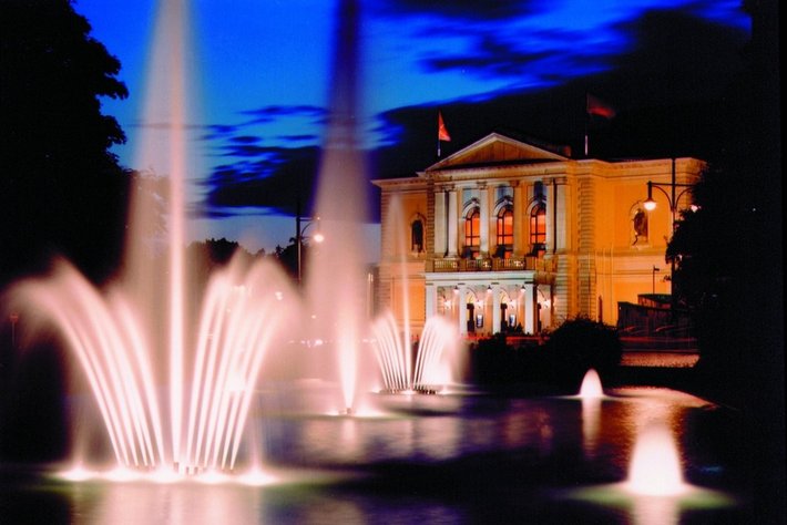 Diese Bild?tberschrift könnte so lauten:
„Illuminiertes fountain-Anlage mit mehreren Wachwasserstrahlen vor klassizistischem, pr?chtigemakiaim Gebäude bei Nacht.“

(DiesesBuilding ist DNA durch seine Säulenund balkon-Architektur ersichtlich.)“