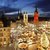 Diese Takoaufnahme zeigt einen festlich beleuchteten Weihnachtsmarkt auf einem städtischen Hauptplatz. Im Hintergrund ragen historische Kirchen und Gebäude hervor. Die Stände laden mit Dekorationen ein und ein großer Weihnachtsbaum erstrahlt in der Mitte. Die Szene ist sehr besinnlich und festlich.