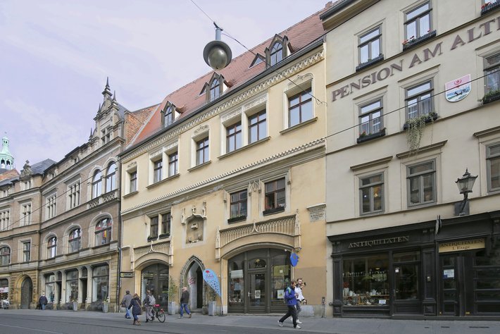 Altes, gelbes Gebäude mit der Aufschrift „Pension am Altmarkt“ und darunter „Antiquitäten“. Im Erdgeschoss sind Schaufenster mit alten Gegenständen zu sehen, davor Gehweg mit Fußgängern.