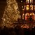 Ein wunderschön geschmückter Weihnachtsbaum, der mit kleinen Lichtern erleuchtet ist, steht im Mittelpunkt. Im Hintergrund ist eine festlich beleuchtete markante Gebäude-Silhouette mit Balkonen und weiteren Lichtern sowie verzierten Stützpfeilern zu sehen. Die Szene wirkt festlich und weihnachtlich und wird von Menschen durchlaufen.