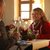 Zwei Personen sitzen an einem Tisch mit Wein- und Wassergläsern, essen gemeinsam und unterhalten sich freundlich. Auf dem Tisch liegen Servietten und eine Blume in einer Vase.