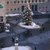 In diesem Großstadtplatz steht ein großer, mit Schnee bedeckter Weihnachtsbaum. Menschen gehen um ihn herum, die Fußwege sind teilweise vereist und eisglatt. Festliche Atmosphäre mit Weihnachtsstimmung in einer Innenstadtumgebung.