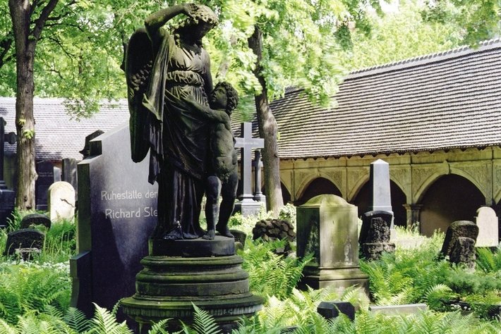 Diese Fotografie zeigt ein Grabdenkmal in einem Parkfriedhof: Eine Frauengestalt, die ein Kind hält. Die Figur wirkt traurig und elegant. Daraufhin steht eine Inschrift, die an den berühmten deutschen Schriftsteller Richard Steffen erinnert.