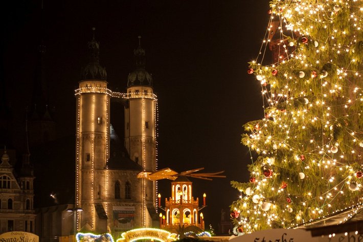 Ein beleuchteter Weihnachtsbaum mit vielen Lichtern ist vor einem im Dunkeln mähnlichen zu sehen, vermutlich eine Kathedrale oder Kirche.

Dominant sind die beleuchteten Türme mit typischen Spitzen.

Frohe Weihnachtsstimmung liegt in der Luft.?????